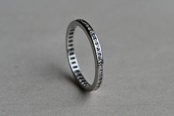 A classic platinum eternity band with forty-two (42) single cut diamonds tucked in a channel. Crisp, à jour setting. Ring standing upright on gray paper background.