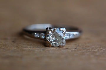 close up photo of old European cut diamond.  This ring is die-struck and channel set with four fresh-faced, single cut diamonds — two at each shoulder. The primary diamond is stunning, with a large culet and small table that collectors love to see in old cut diamonds. The gem is set in a square head with fishtail prongs at each corner. It has a modest, practical rise from the shank (just over 4.5mm) and the ring as a whole has a nice, low profile.