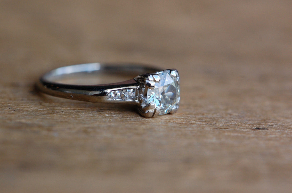 close up photo of side of old European cut diamond. This ring is die-struck and channel set with four fresh-faced, single cut diamonds — two at each shoulder. The primary diamond is stunning, with a large culet and small table that collectors love to see in old cut diamonds. The gem is set in a square head with fishtail prongs at each corner. It has a modest, practical rise from the shank (just over 4.5mm) and the ring as a whole has a nice, low profile.