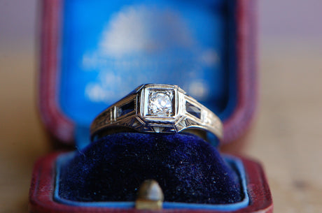 A handsome ca. 1920s Art Deco ring in 20K white gold (!) with an Old European Cut diamond primary and flanking sapphire baguettes. The hand-engraved details are exceptional and appear throughout the mounting. Split leaf motifs up the shoulders, milgrain around the baguettes, and etchings around the head are a few or our favorite accents. 