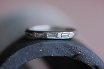 A perfect platinum and diamond baguette wedding band engraved for the year 1949. The band is slim and trim with knife edge shoulders and a trio of flush-set baguette diamonds (.18 ctw, VS/G-H). This ring has the gorgeous patina of 70+ years. A beautiful pair to an engagement ring or simply a sentimental stacking band. Ring photographed from front. Ring laying on top of a black ceramic arch.