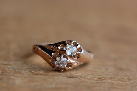 A stunning ca. 1900s toi-et-moi style ring with old mine cut diamonds in a 14K belcher setting. The diamonds are true old miners, with irregular facets, pillow-shaped perimeters, and warm brilliance. They are flush set with claw/belcher prongs and stacked oblique to the ring face. Hand engraved texturing and details on the shoulders. Unusual and wonderful! Ring photographed laying on top of wood with grain.