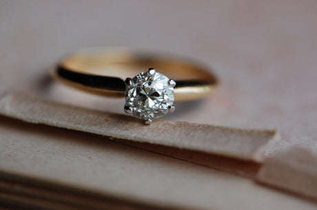 close up photo of solitaire diamond ring. Diamond is set in a platinum 6 prong head with a 14k gold knife edge band. Ring is laying down on cream colored paper.
