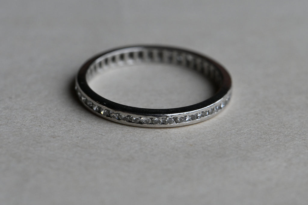 A classic platinum eternity band with forty-two (42) single cut diamonds tucked in a channel. Crisp, à jour setting. Ring laying on gray paper background.
