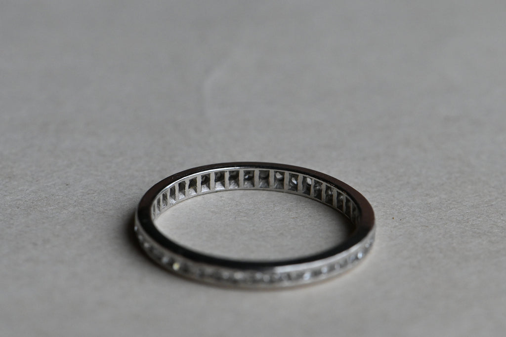 A classic platinum eternity band with forty-two (42) single cut diamonds tucked in a channel. Crisp, à jour setting. Ring laying on gray paper background.