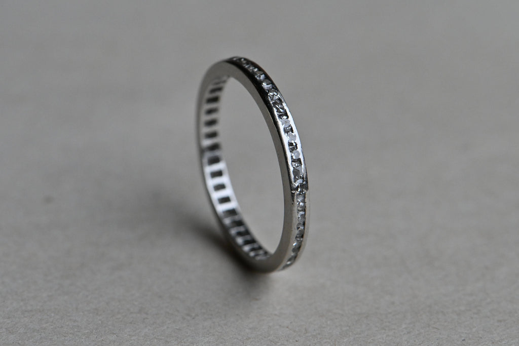 A classic platinum eternity band with forty-two (42) single cut diamonds tucked in a channel. Crisp, à jour setting. Ring standing upright on gray paper background.