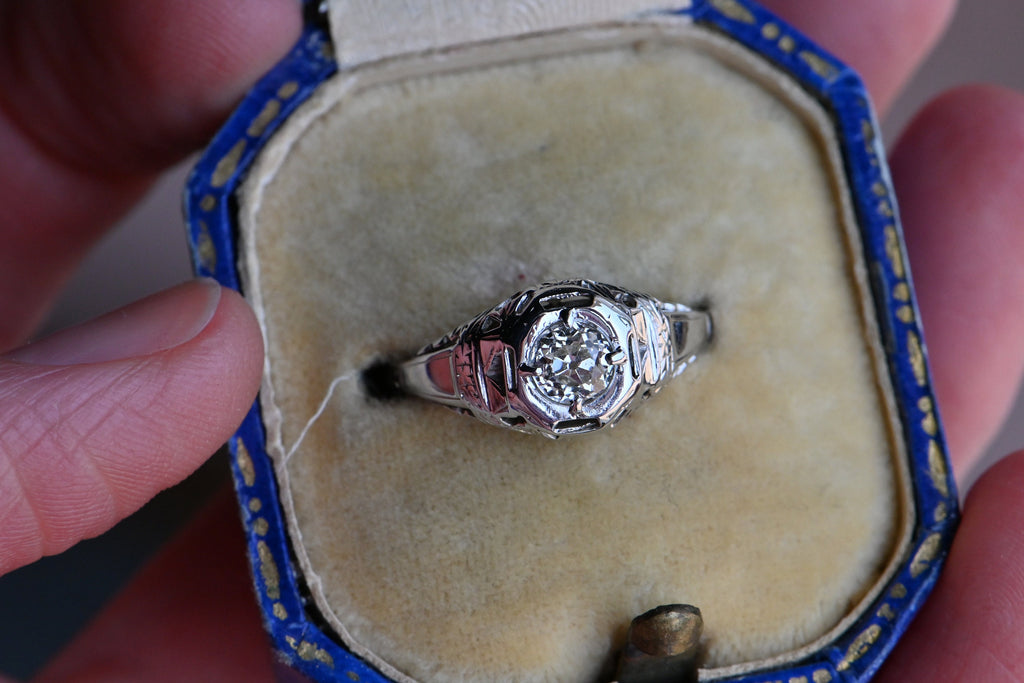 Art Deco engagement ring! This ring has hand-sawed filigree details and a juicy old mine cut feature stone. The 18K white gold mounting has engraved details on every millimeter, including bridal wreaths down the sides of the slim shank. Ring  inside  cream and blue vintage ring box.
