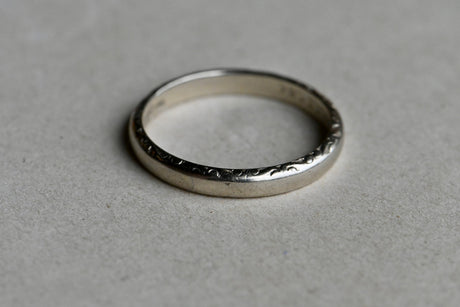 A simple Art Deco wedding band with just enough detail to tug at your heart! One edge of this 14K white gold band is chased and the other is plain, a thoughtful details for a bride planning to wear the band against an engagement ring. The interior is engraved with the name of the original couple and their wedding date May 22nd, 1921. Made in NYC in the 1920s by Harry Abel. 