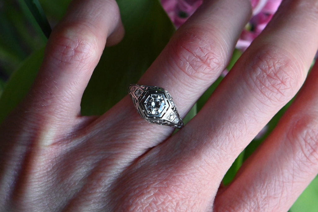 A classic Art Deco solitaire ring with a .45 carat Old European Cut diamond set in 18K white gold filigree.The diamond is flush-set in a floating, hexagonal head. This diamond is lively and crisp, graded VS2/G. Close up of  ring modeled on female hand.