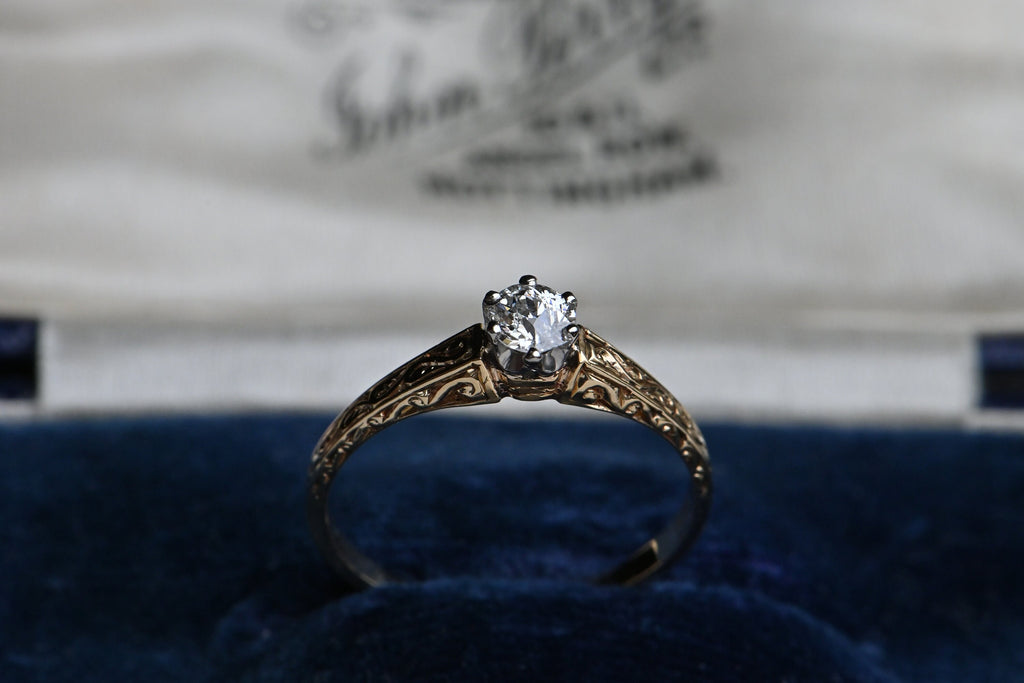 An elegant ca. 1920s diamond solitaire ring with a beautiful mounting. The 14K ring has hand-engraved foliate details on three sides of the shoulders, gently tapering to a smooth, plain shank. The beveled, densely chased shoulders frame a gorgeous, century-old diamond (VS1/G) held in a low-profile prong head
