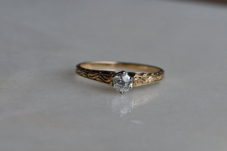 An elegant ca. 1920s diamond solitaire ring with a beautiful mounting. The 14K ring has hand-engraved foliate details on three sides of the shoulders, gently tapering to a smooth, plain shank. The beveled, densely chased shoulders frame a gorgeous, century-old diamond (VS1/G) held in a low-profile prong head