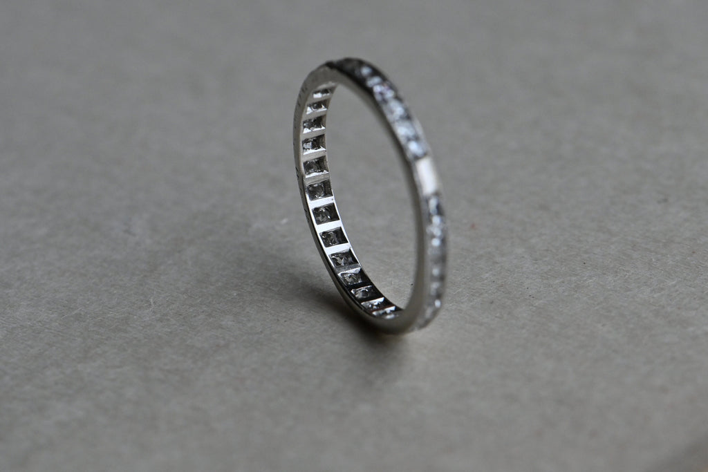 An Art Deco platinum eternity band engraved for a wedding on 4-3-20 … this ring is 102 years old! The band is channel set with thirty-four (34), à joured single cut diamonds, .75 CTW. Milgrain edging and a single "blank" space. Slim and elegant for stacking or pairing with an engagement ring. Engraved on one edge with "W.E.W. Jr. and D.Q. 4-3-20.” Outstanding condition. 