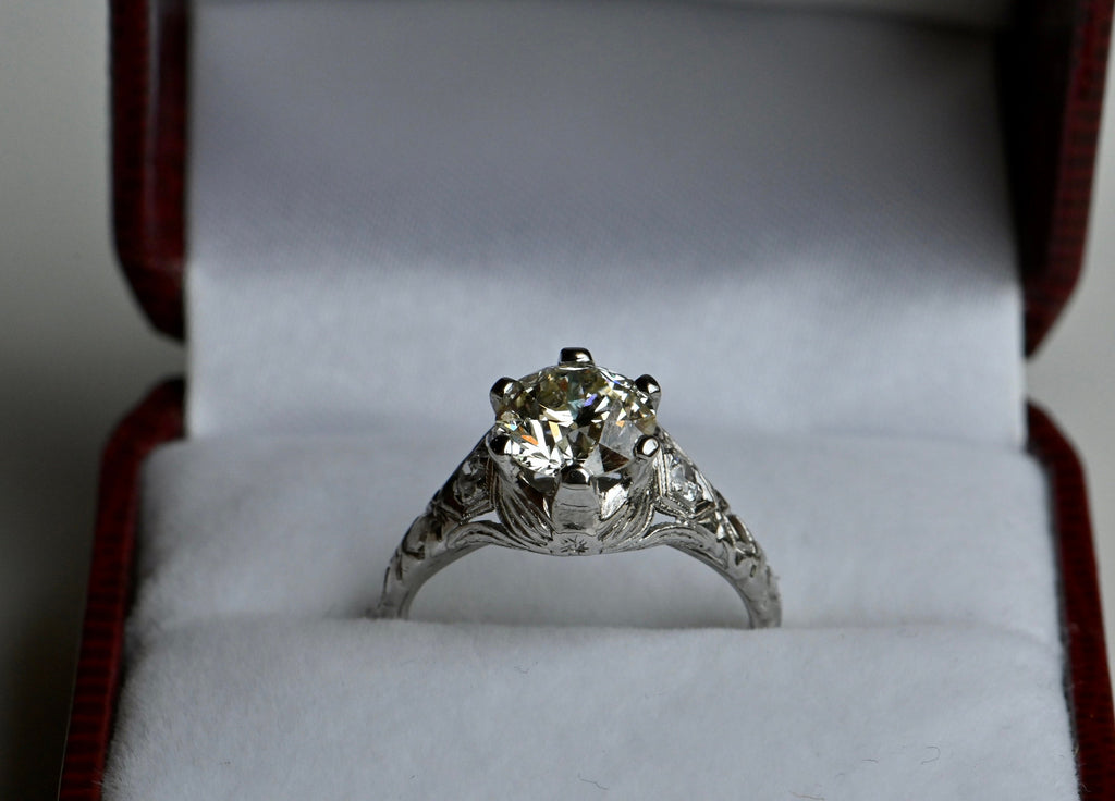 A 1.55 carat old-style circular cut diamond perched in a substantial, hand engraved platinum mounting. This stone has a lovely spread (7.36-7.46mm) and a hint of color, like a fine champagne. Ring in antique ring box.