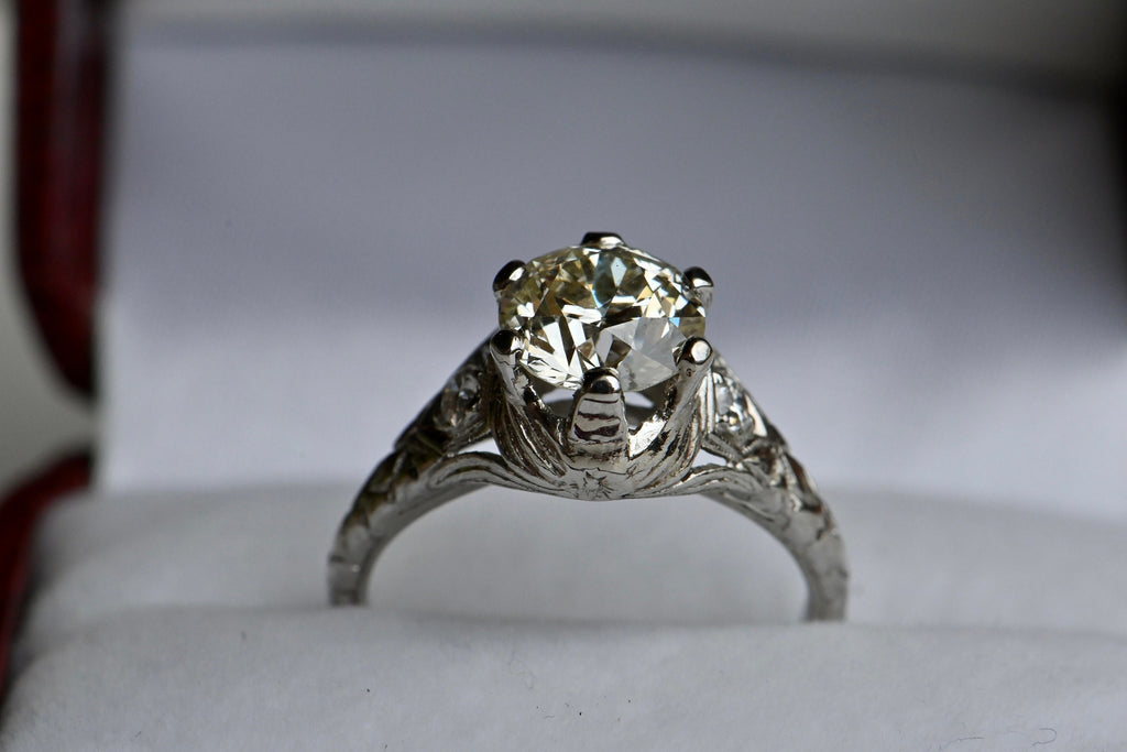 A 1.55 carat old-style circular cut diamond perched in a substantial, hand engraved platinum mounting. This stone has a lovely spread (7.36-7.46mm) and a hint of color, like a fine champagne.  Ring in antique ring box.