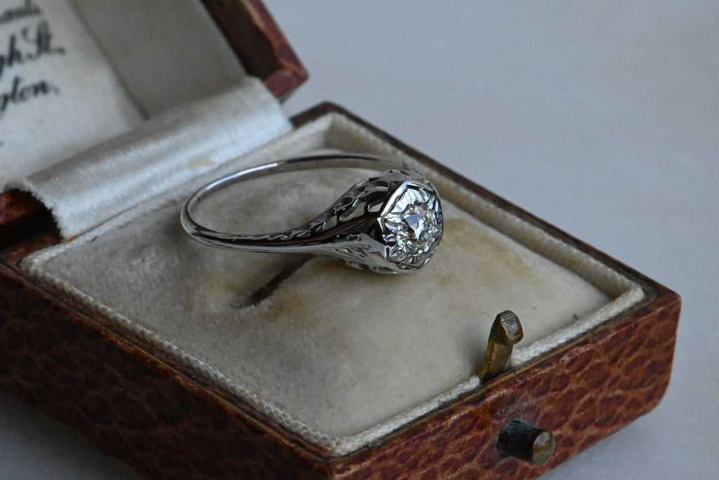 An Art Deco 18K diamond engagement ring with an Old European Cut diamond tucked in a hexagonal head.  Ring inside of antique ring box with cream velvet lining.